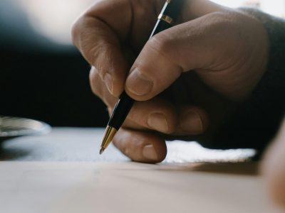 Detail shot of a hand holding a pen, writing on paper with blurred background.